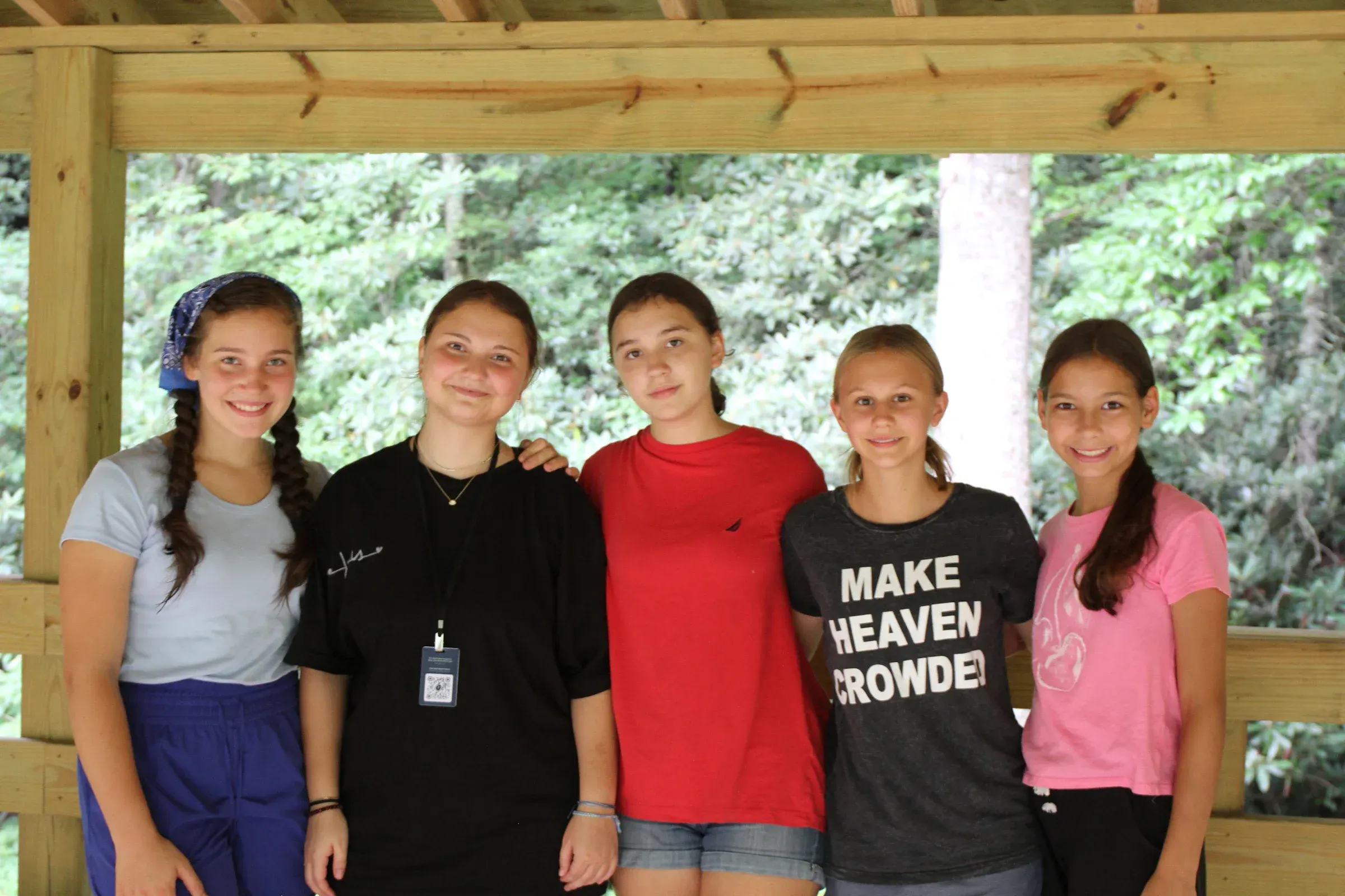 Five campers smile together on a wooden cabin porch.