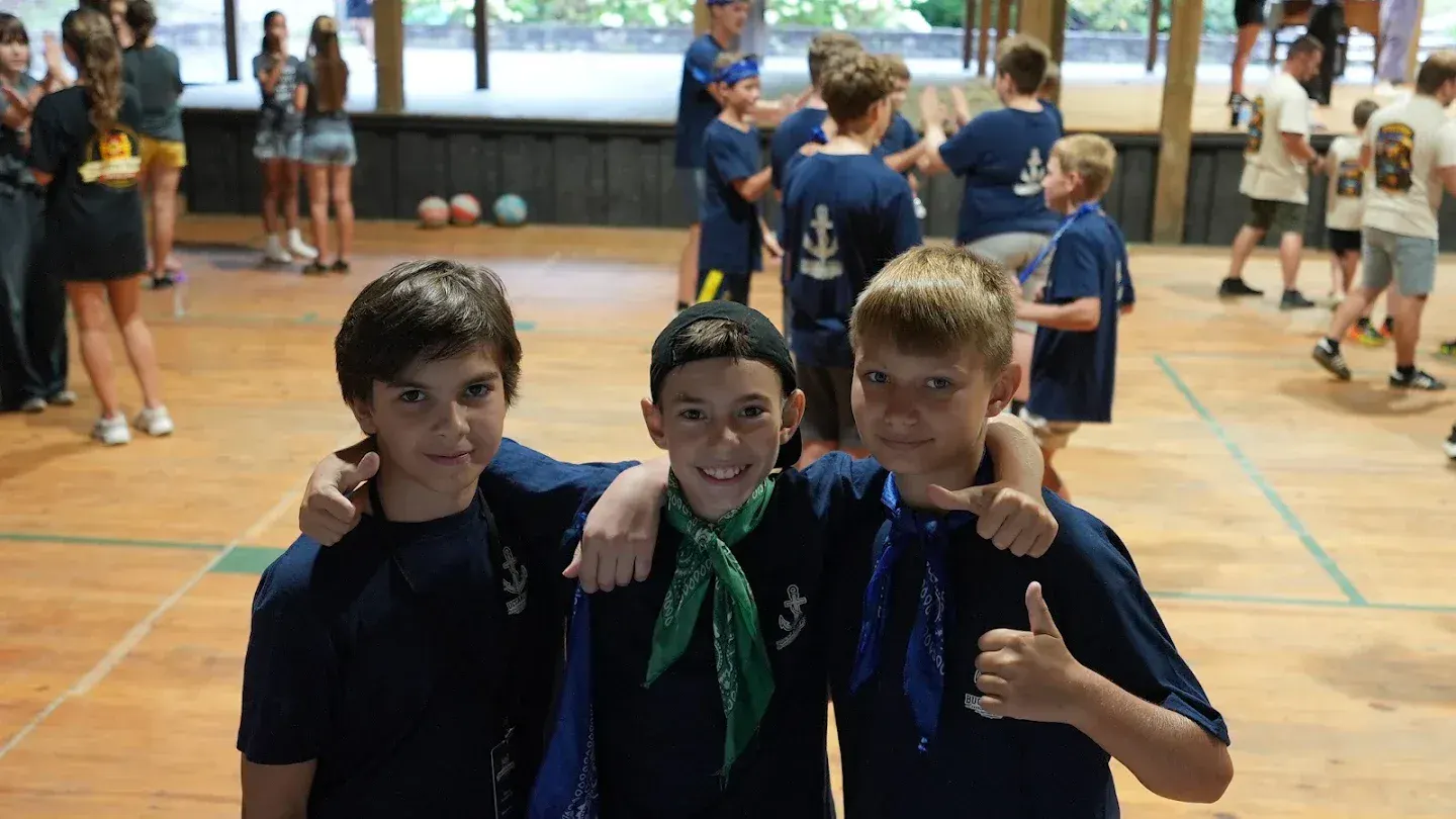 Three boys in team bandanas stand arm in arm and smile in the pavilion.
