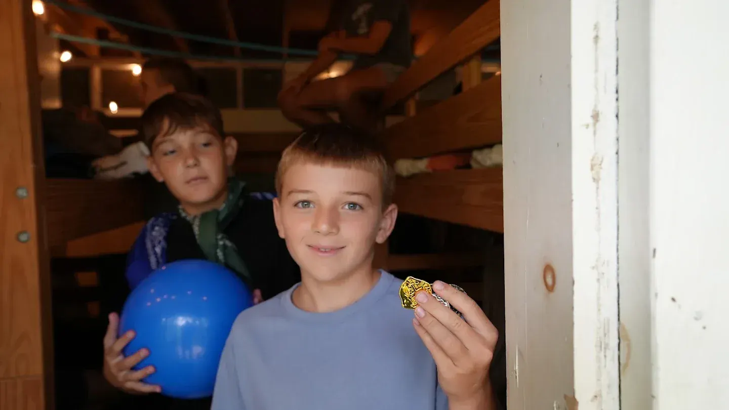 A smiling camper holds up a gold medal in the cabin doorway.